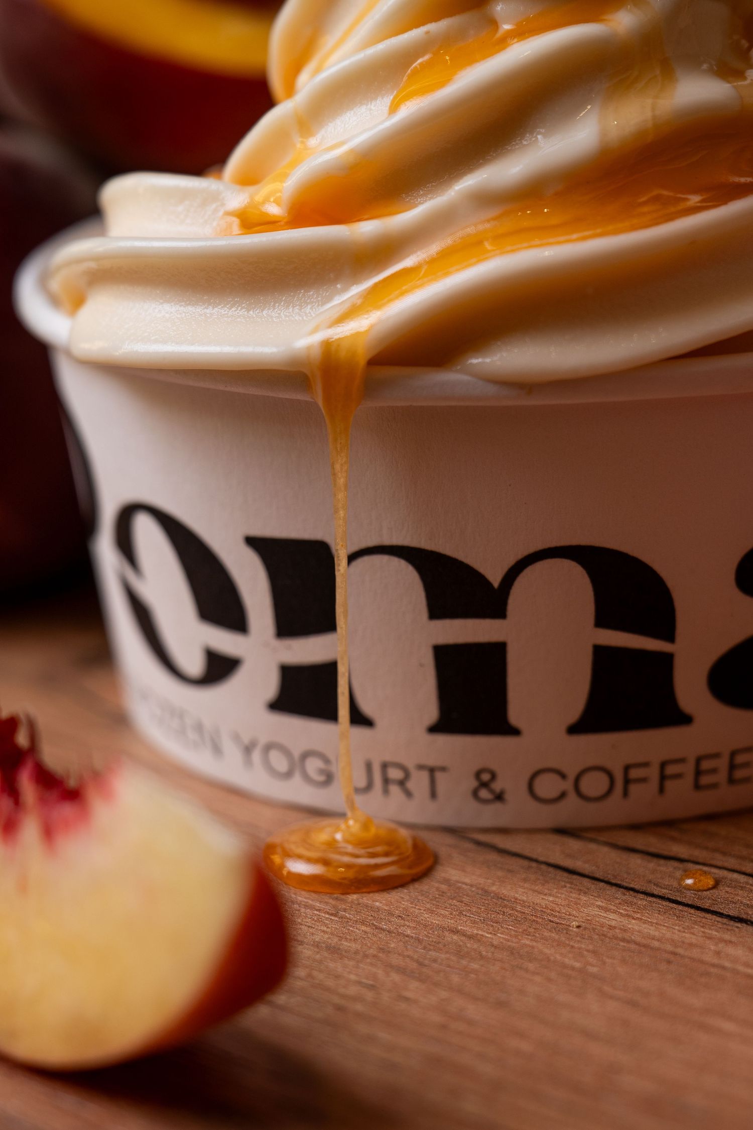 Caramel sauce drizzling over creamy frozen yogurt in a branded cup at Oma Frozen Yogurt & Coffee shop.