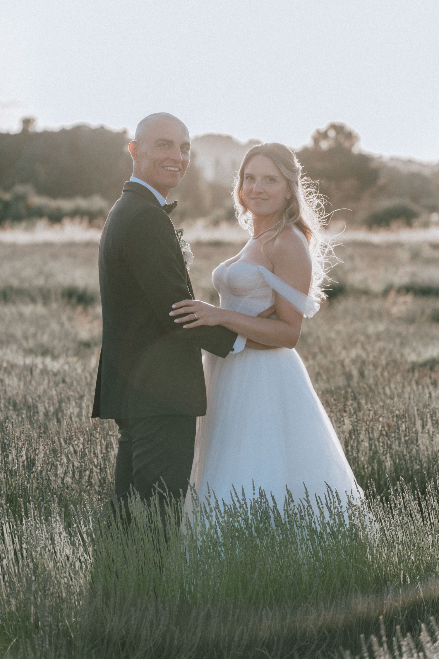 Bride and groom posing in a lavender field at golden hour, bride in off-shoulder tulle gown.