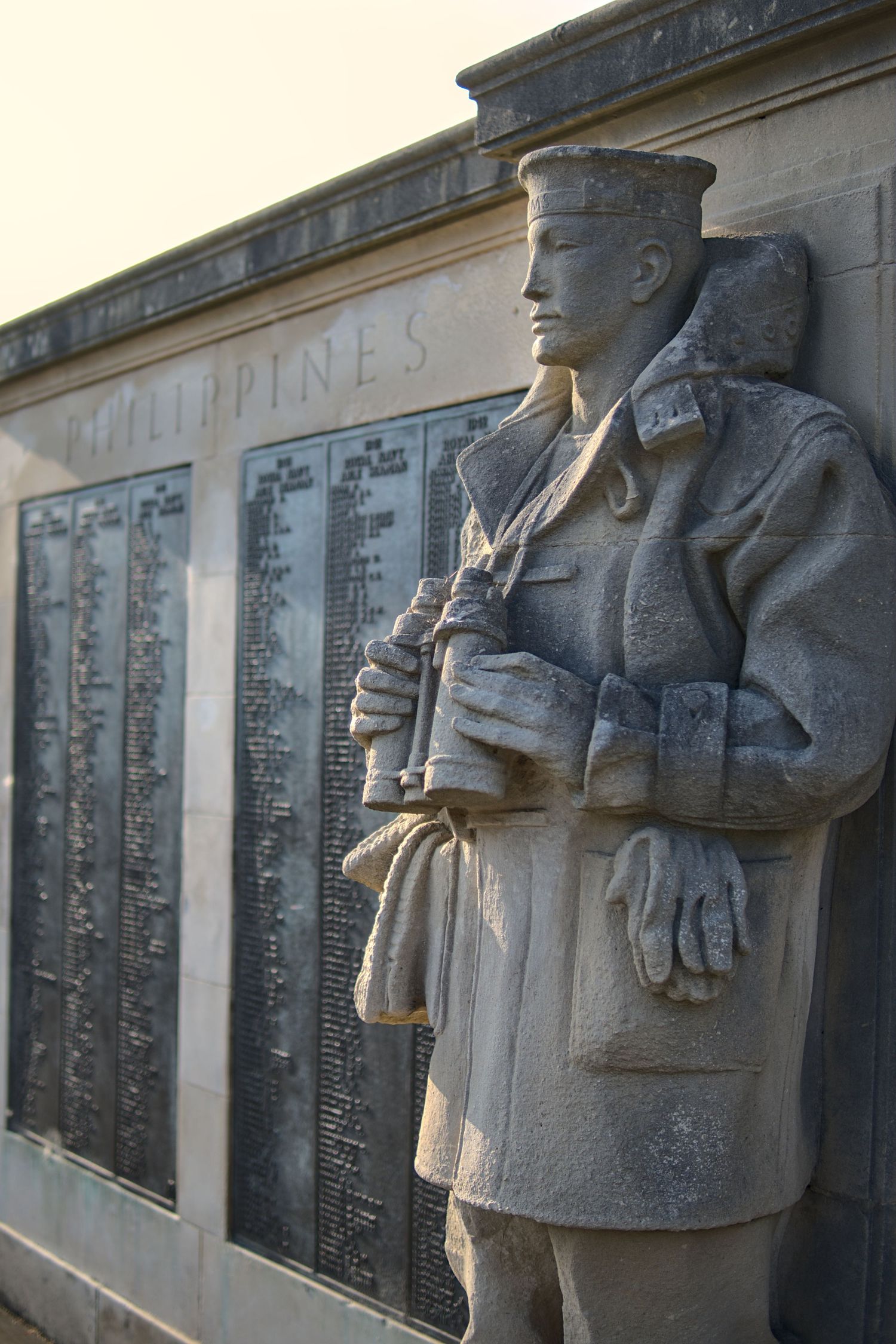 Stone soldier statue stands beside a war memorial wall engraved with Philippines and names.