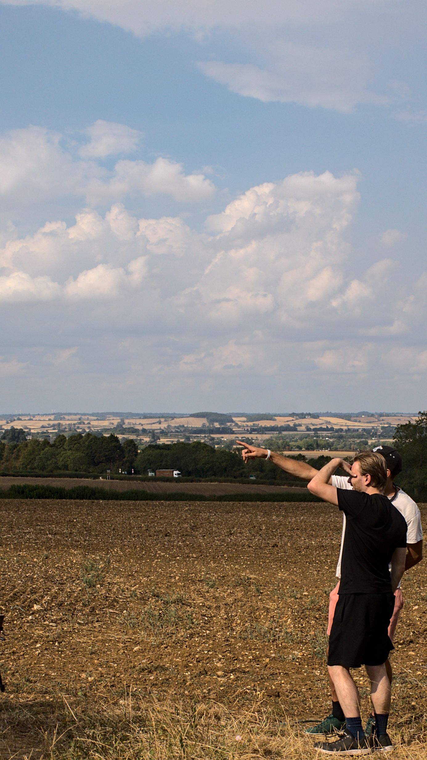 Two people pointing at cumulus clouds over open countryside farmland on a sunny day.