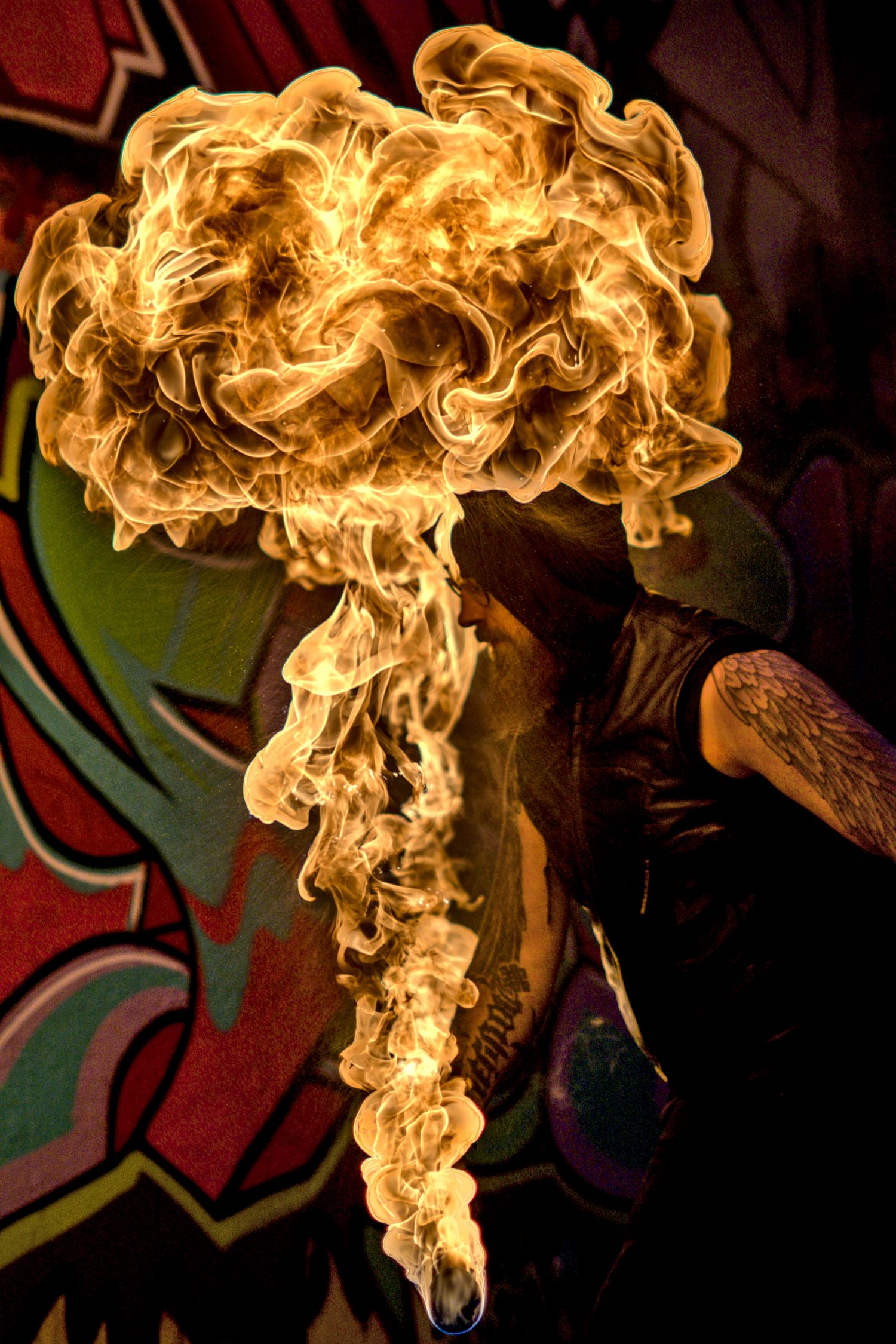 Fire performer creates stunning mushroom cloud fireball against vibrant graffiti backdrop.
