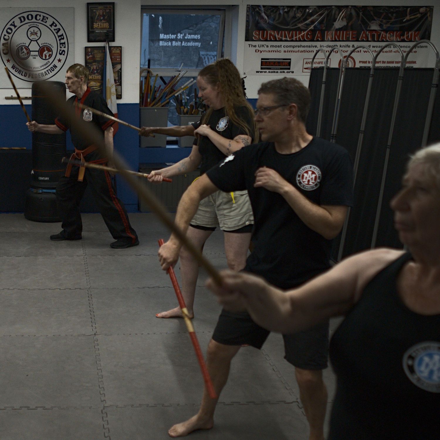 Martial arts students practice stick fighting techniques in a dojo during a group weapons training class.