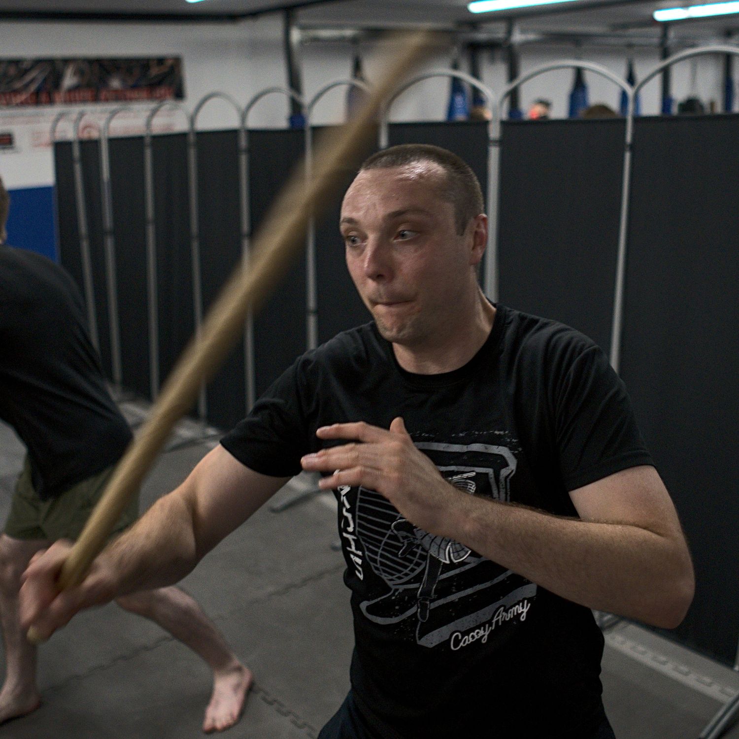 A focused martial artist practices offensive stick fighting moves with a wooden staff indoors.