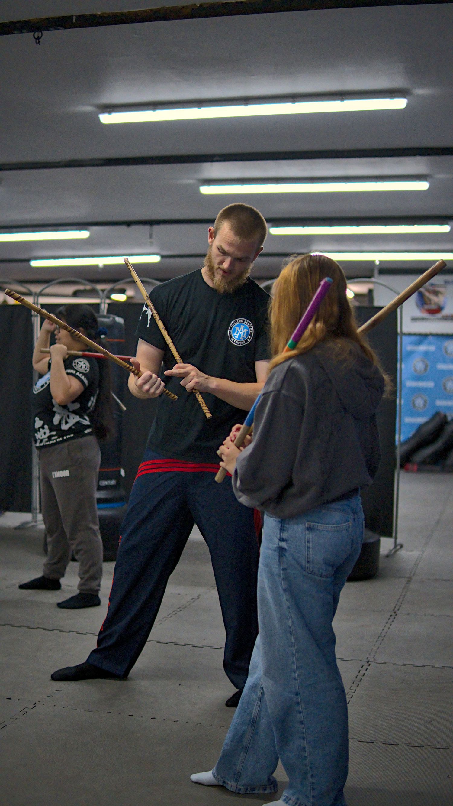 Martial arts instructor teaches a student proper stick fighting techniques during an indoor Arnis training class.