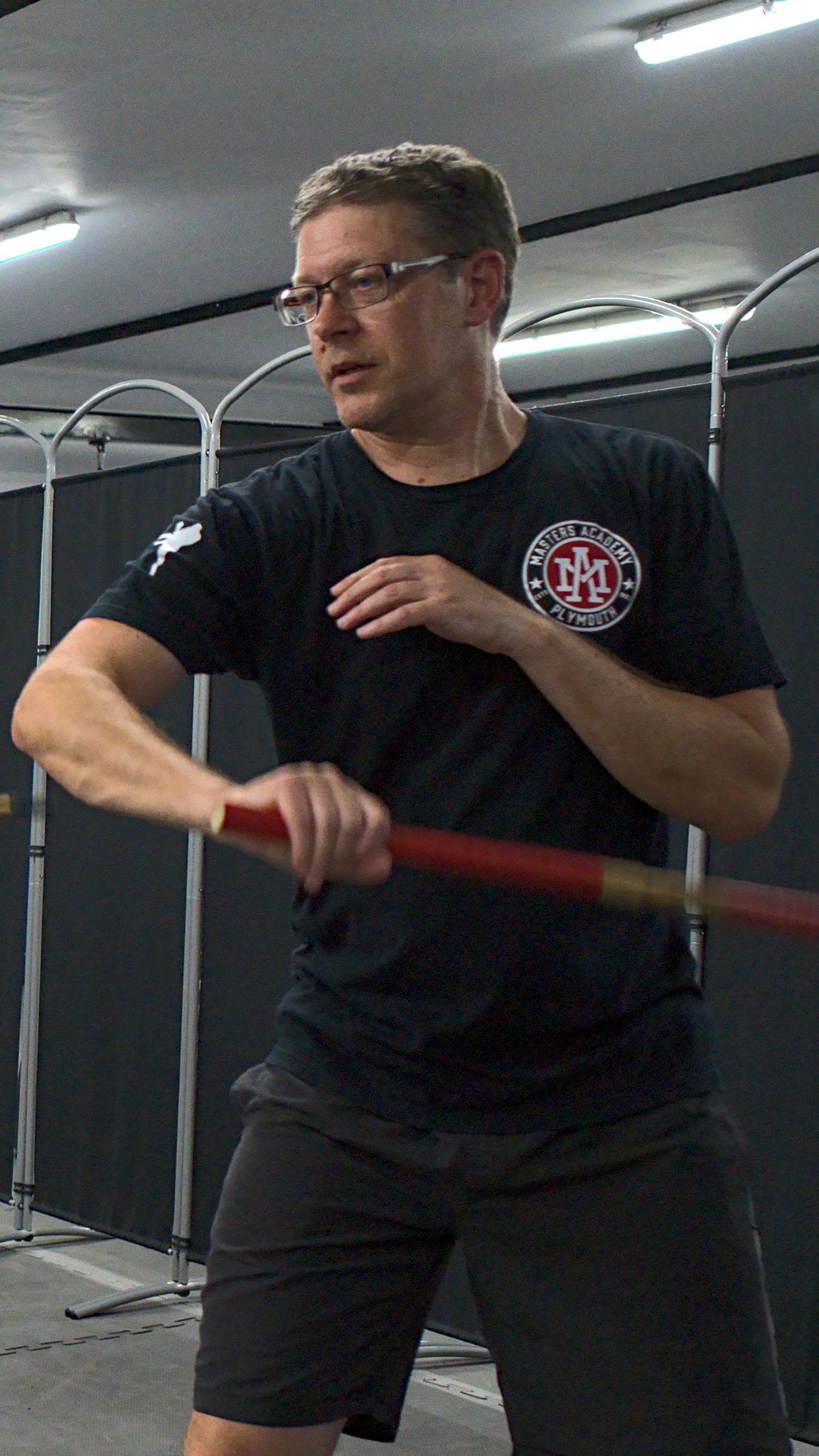 Male martial arts instructor in black uniform practices staff techniques in a training facility.