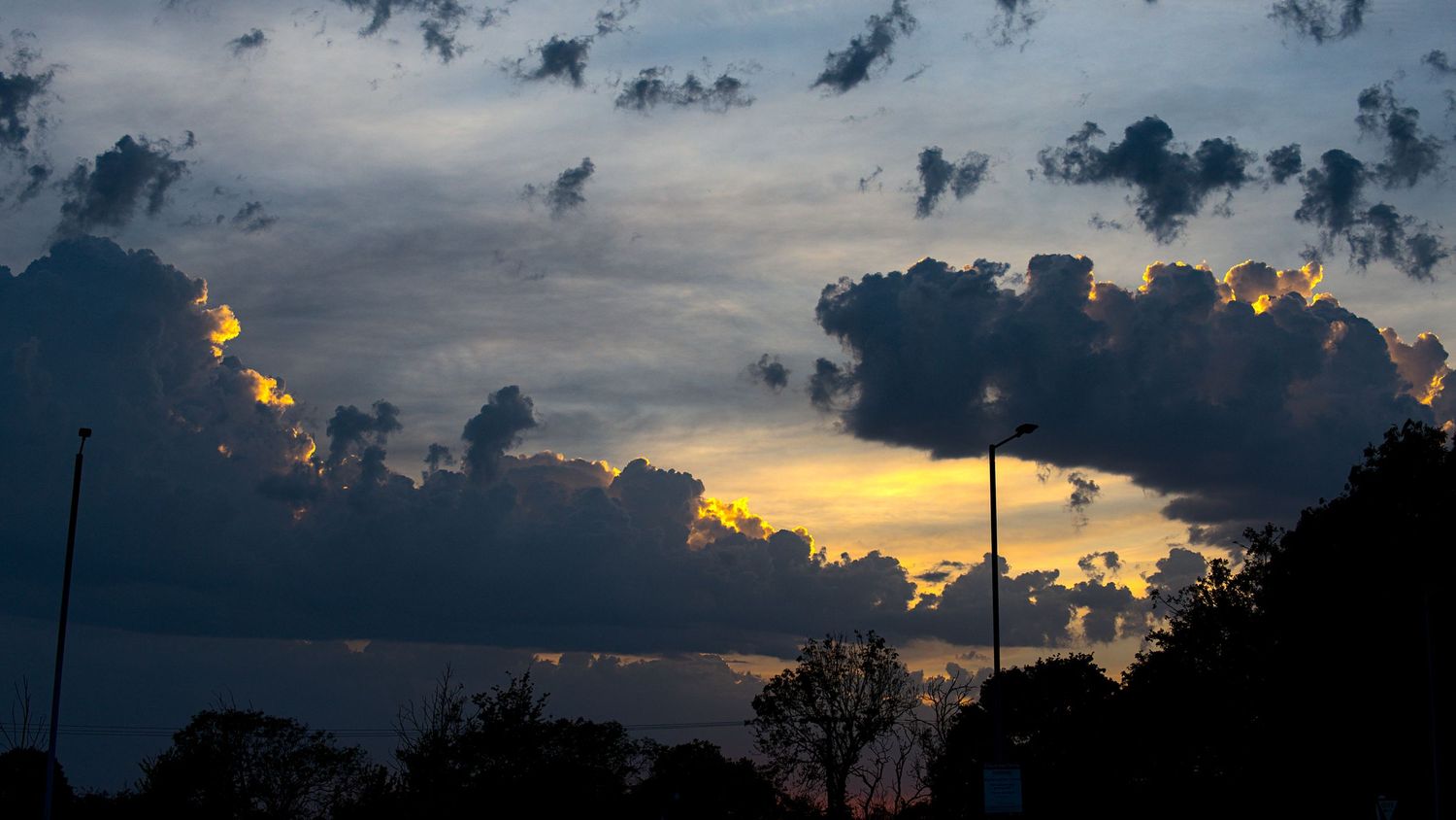 Dramatic sunset sky with dark storm clouds and golden light breaking through at dusk.