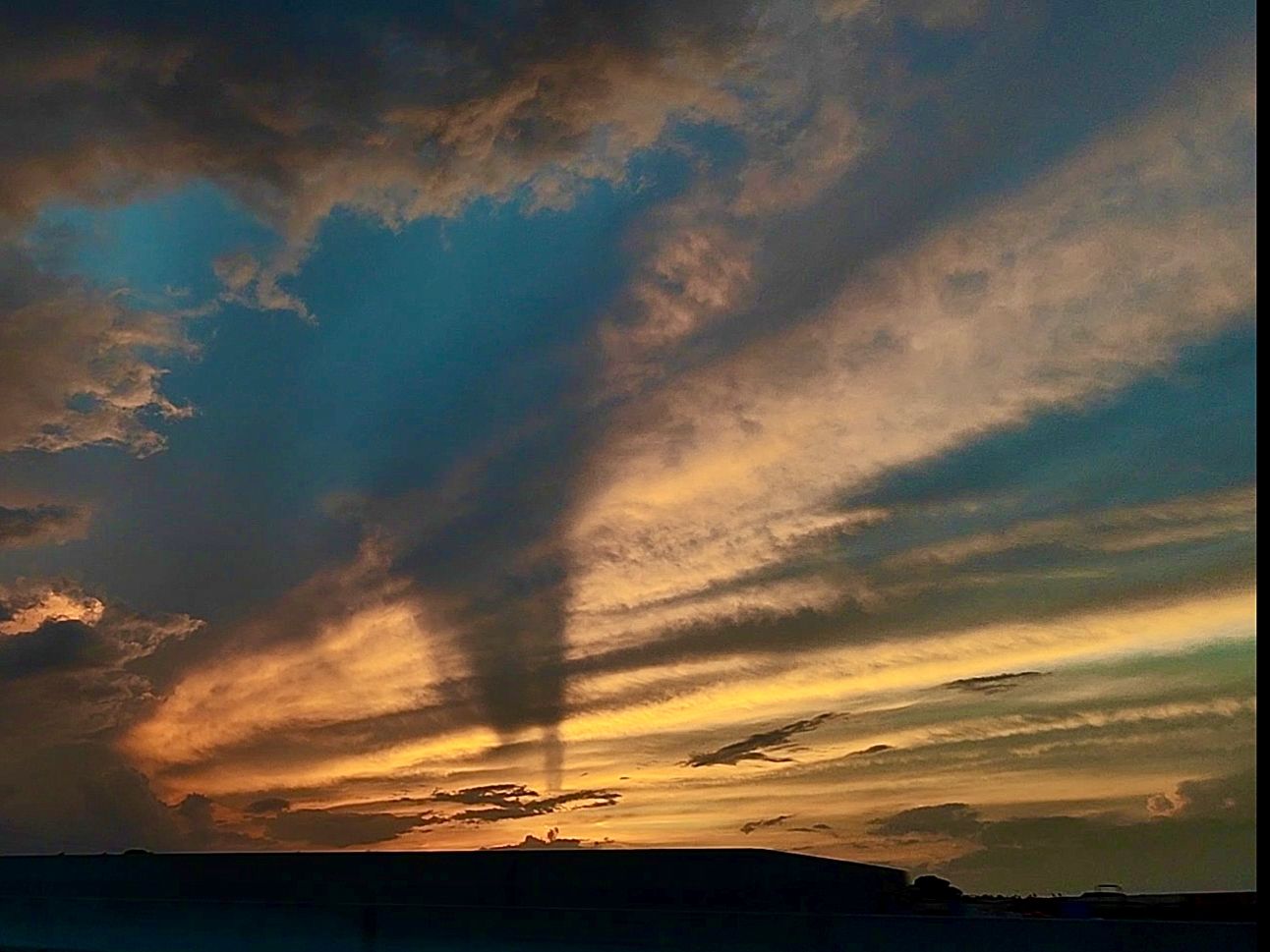 Dramatic golden sunset with crepuscular rays streaming through dark clouds over coastal headland silhouette.