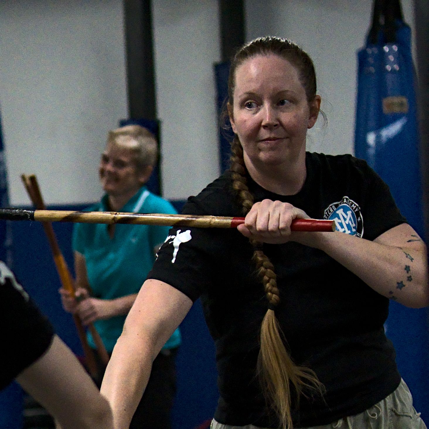 Female martial artist practices Arnis stick fighting with a braided ponytail in a martial arts training gym.
