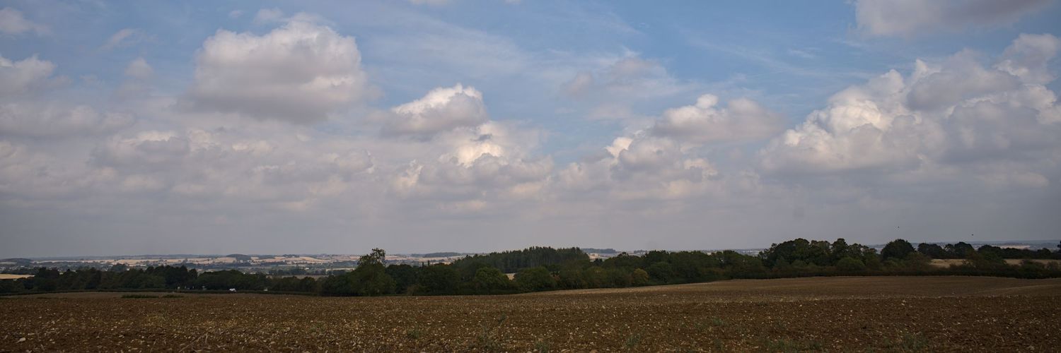 Panoramic view of agricultural farmland under partly cloudy blue sky with distant town on horizon.