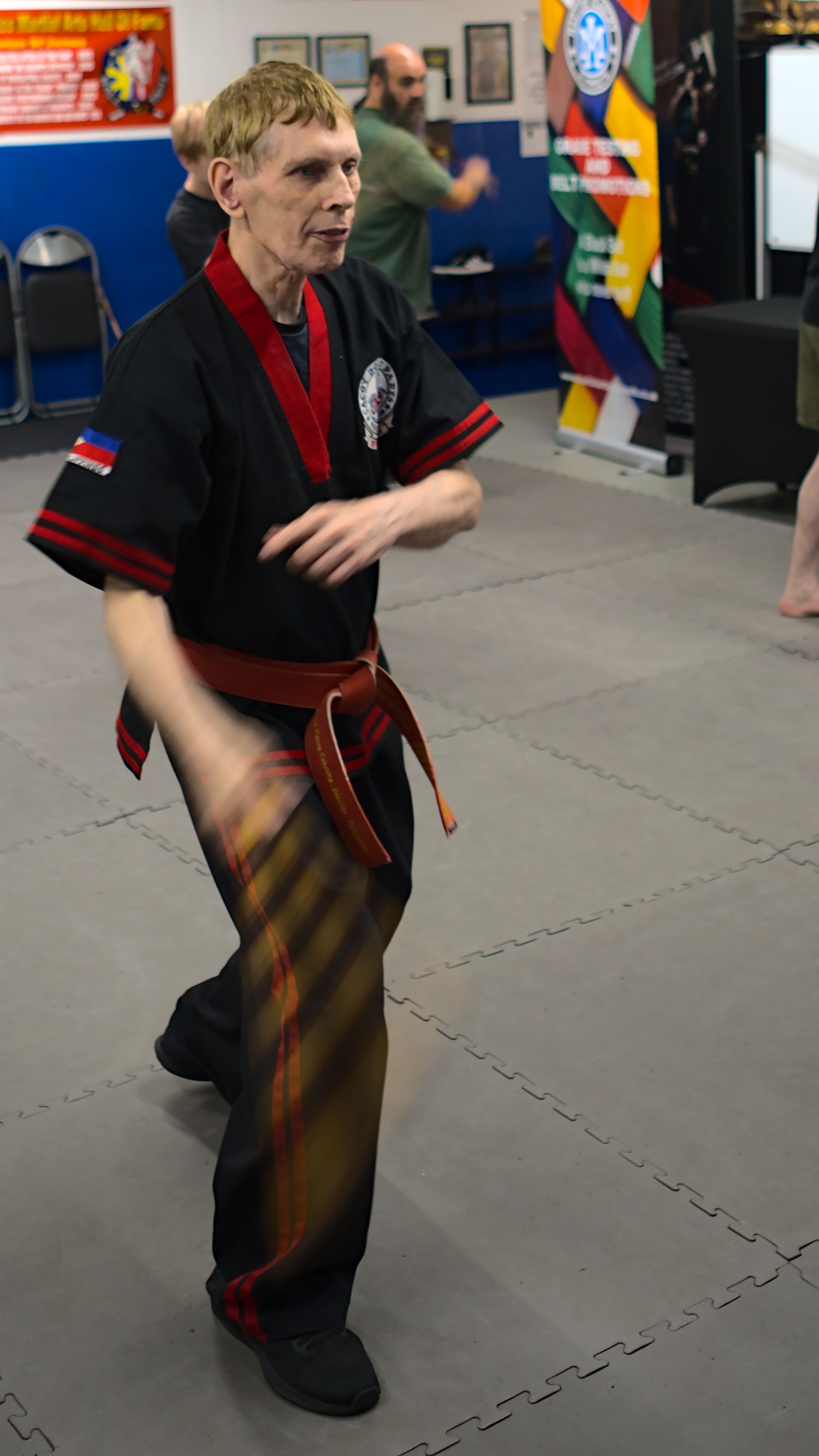 Martial artist in black uniform with red belt performs kata movement during training session at indoor dojo.