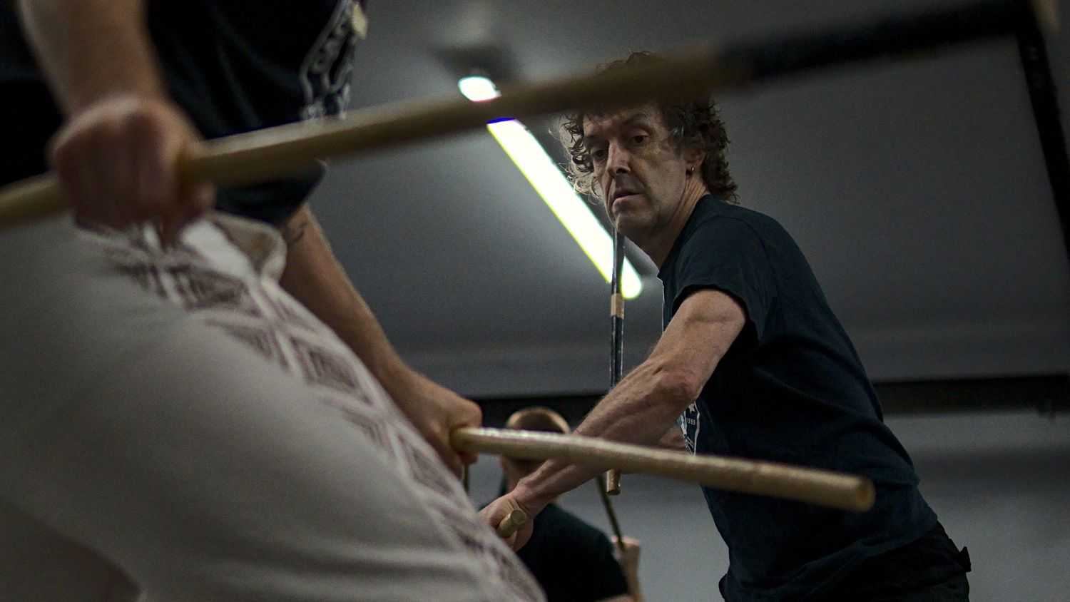Focused martial artist practices stick fighting techniques during an intense Arnis training session in a gym.