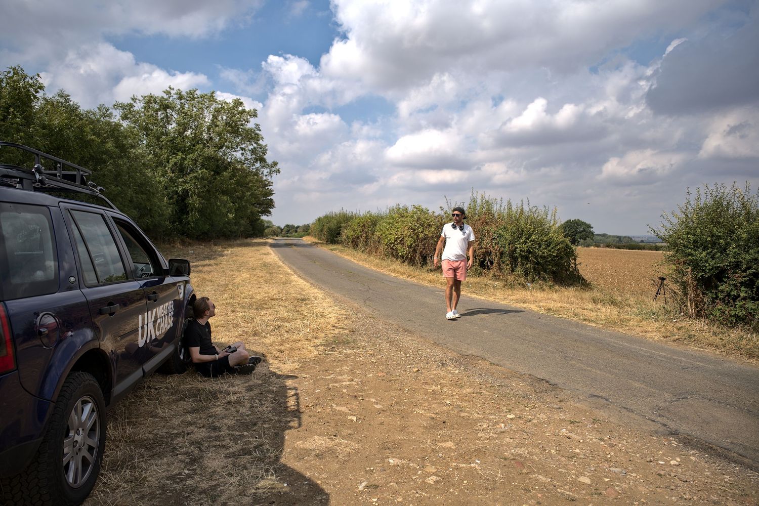 UK Weather Chase vehicle parked on a dry rural road as a person walks toward the camera under cloudy skies.