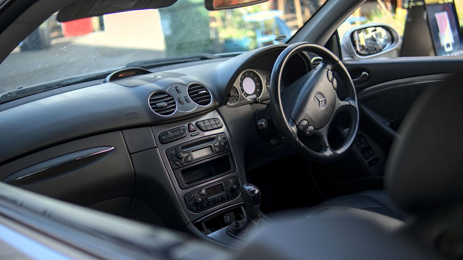 Right-hand drive Mercedes-Benz interior showing steering wheel, dashboard, and center console.