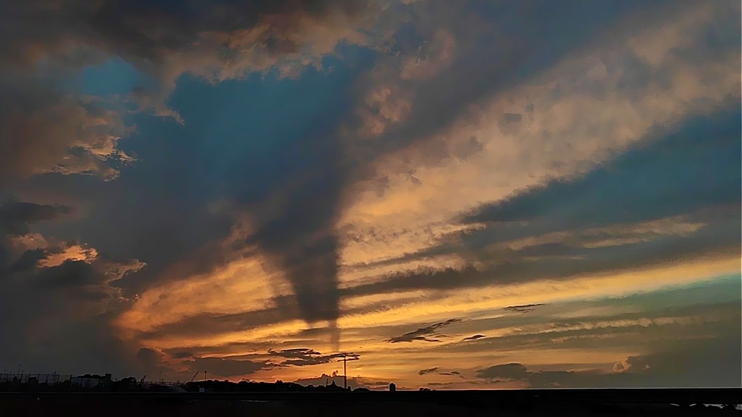 Stunning sunset with dramatic crepuscular rays radiating through dark storm clouds over coastal town silhouette.