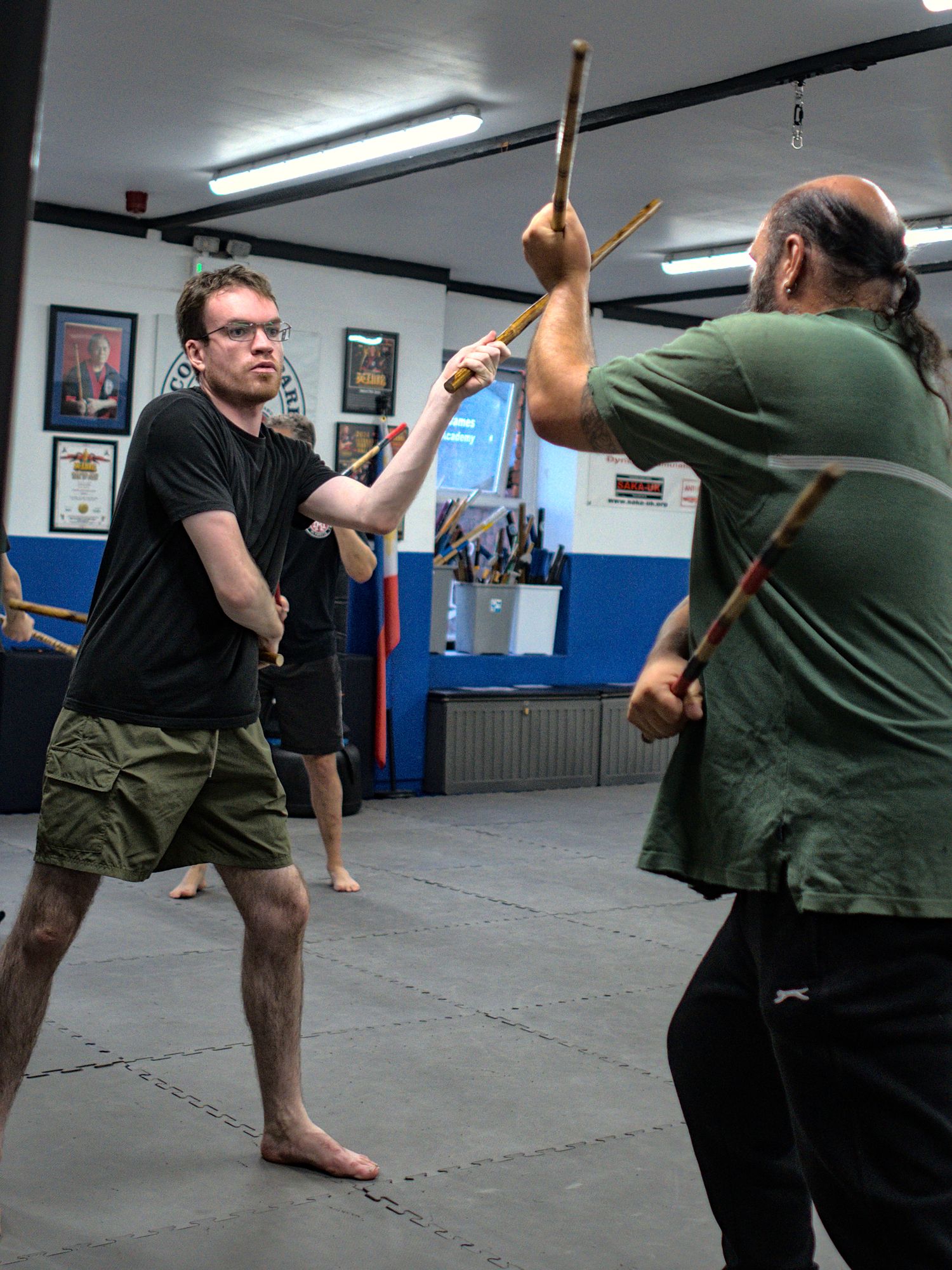 Two students spar with rattan sticks during an Arnis martial arts class indoors.