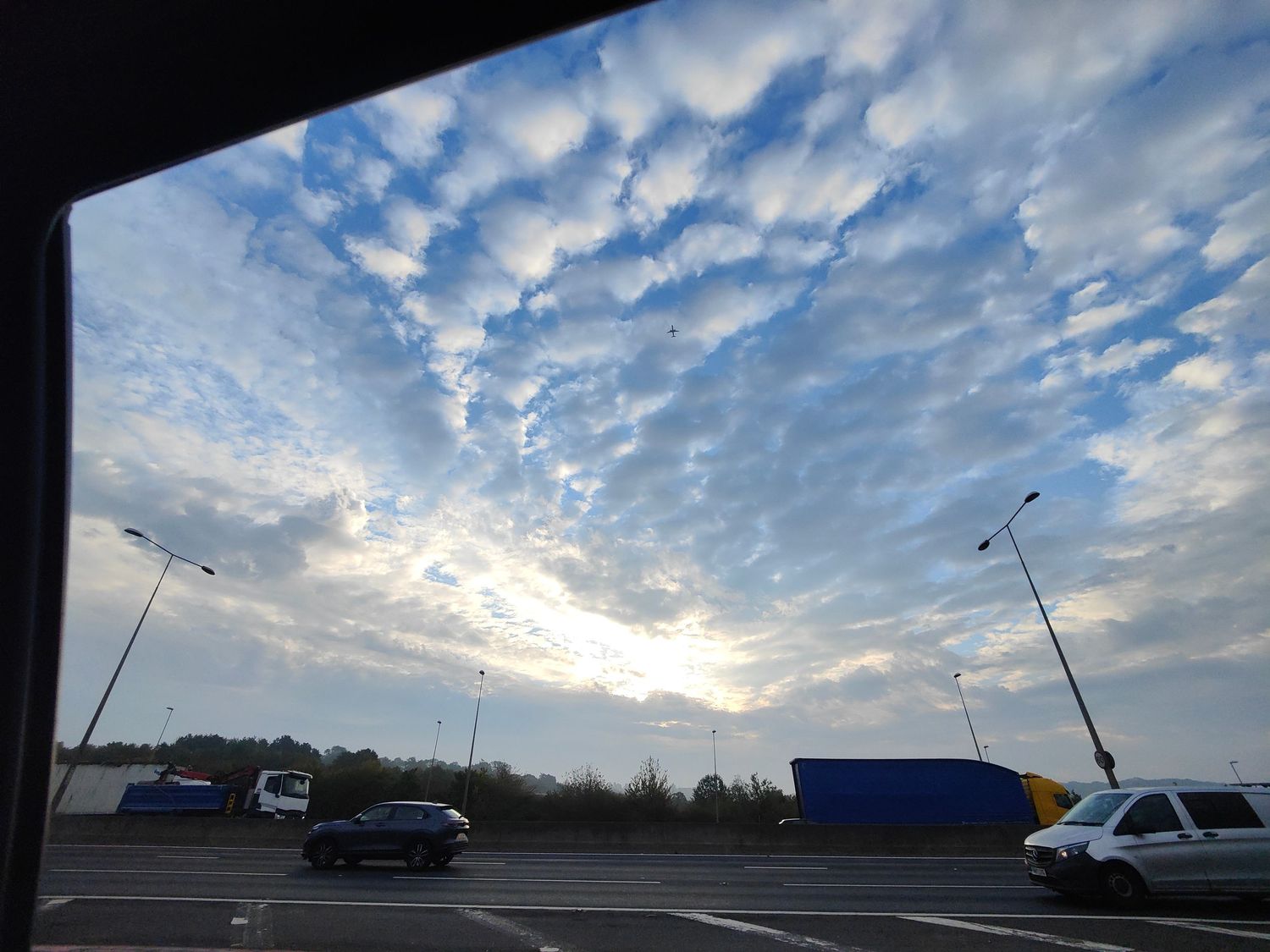 Stunning altocumulus cloud formation at sunset over busy road junction with trucks and cars in traffic.