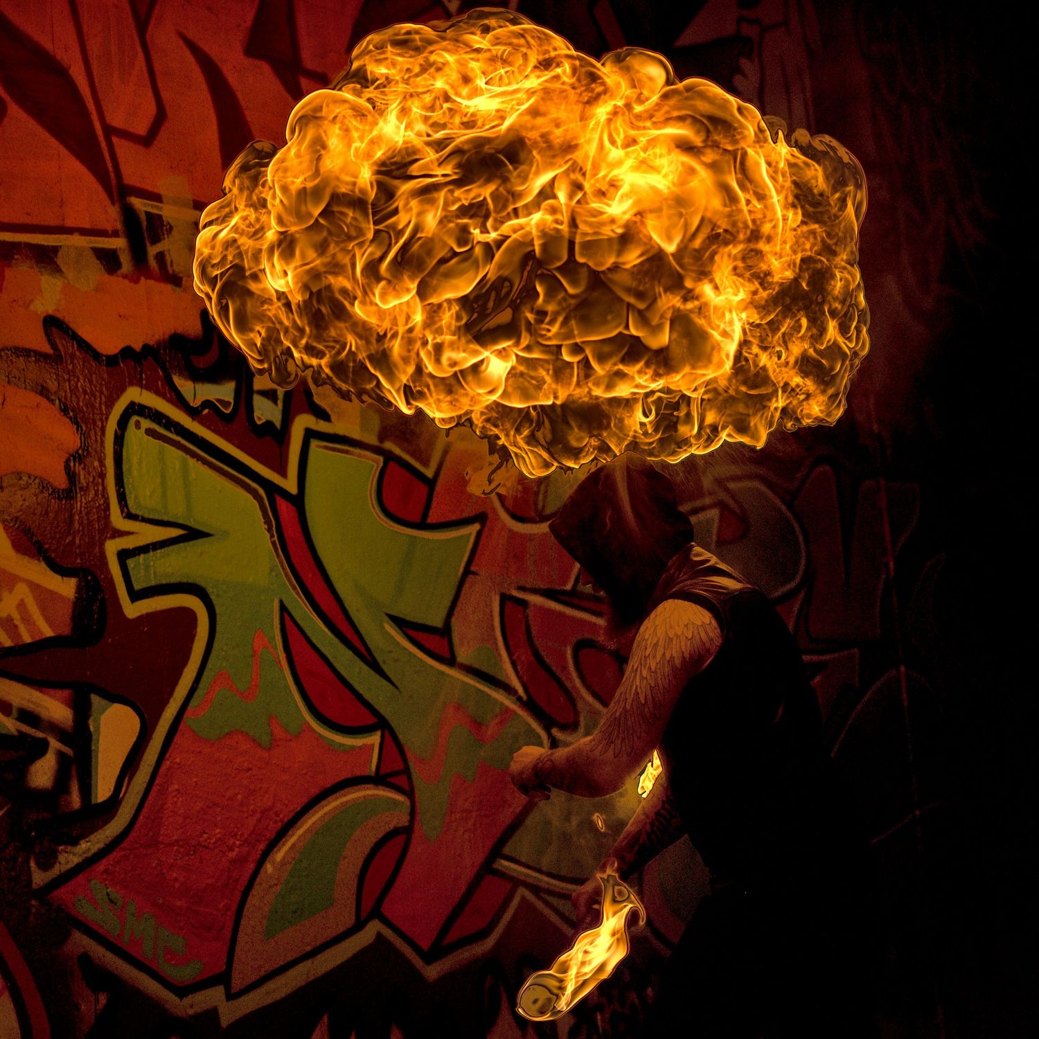 Fire breather creating a massive fireball in front of graffiti wall at night.