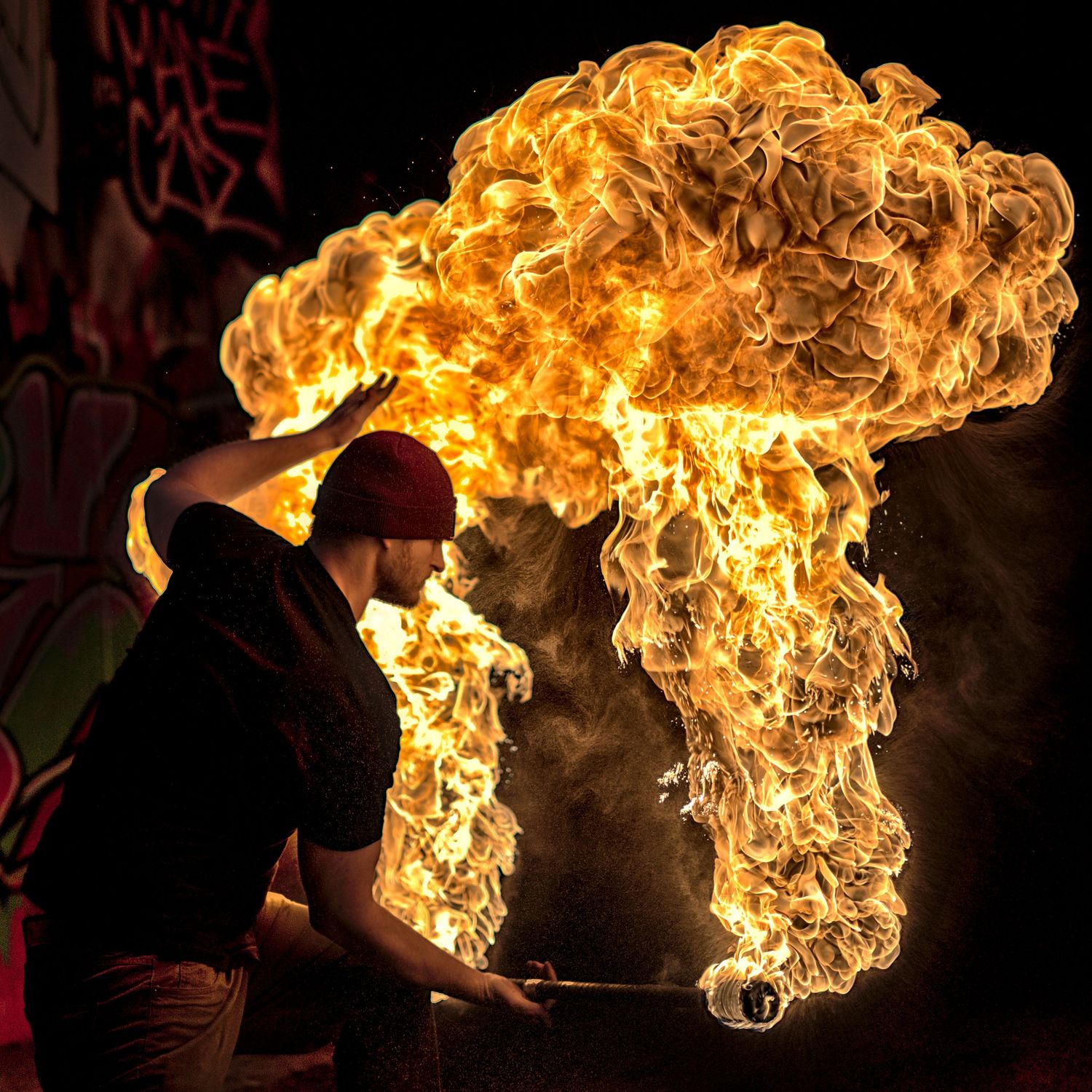Fire performer creates massive mushroom-shaped fireball explosion in dark outdoor setting.