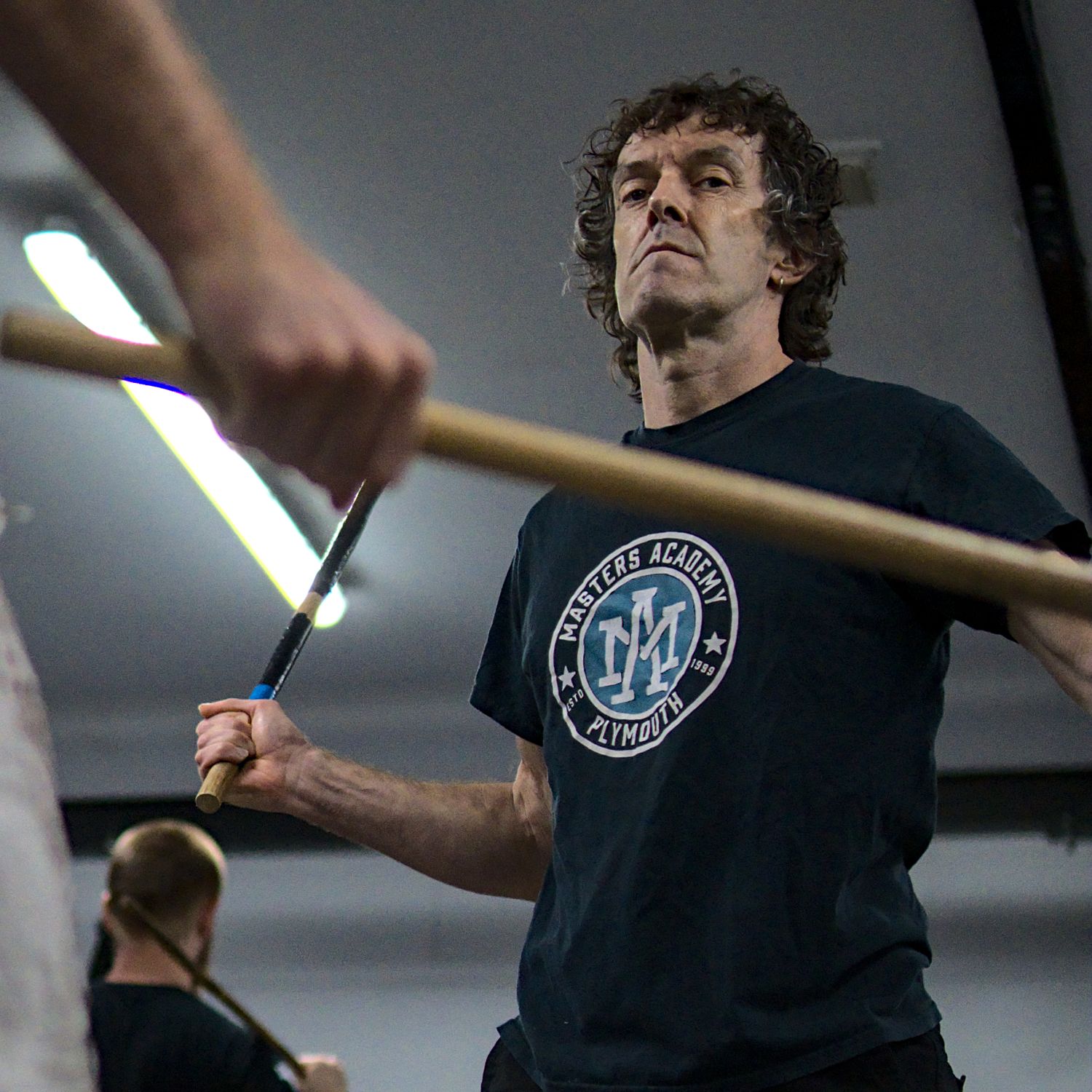 Arnis Academy instructor demonstrates defensive stick fighting techniques during an indoor martial arts training class.