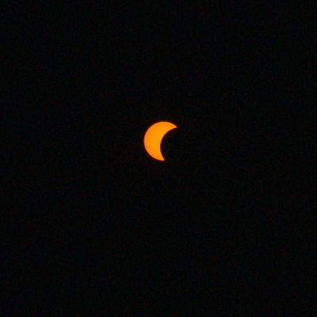 Partial solar eclipse showing orange crescent sun against dark black sky.