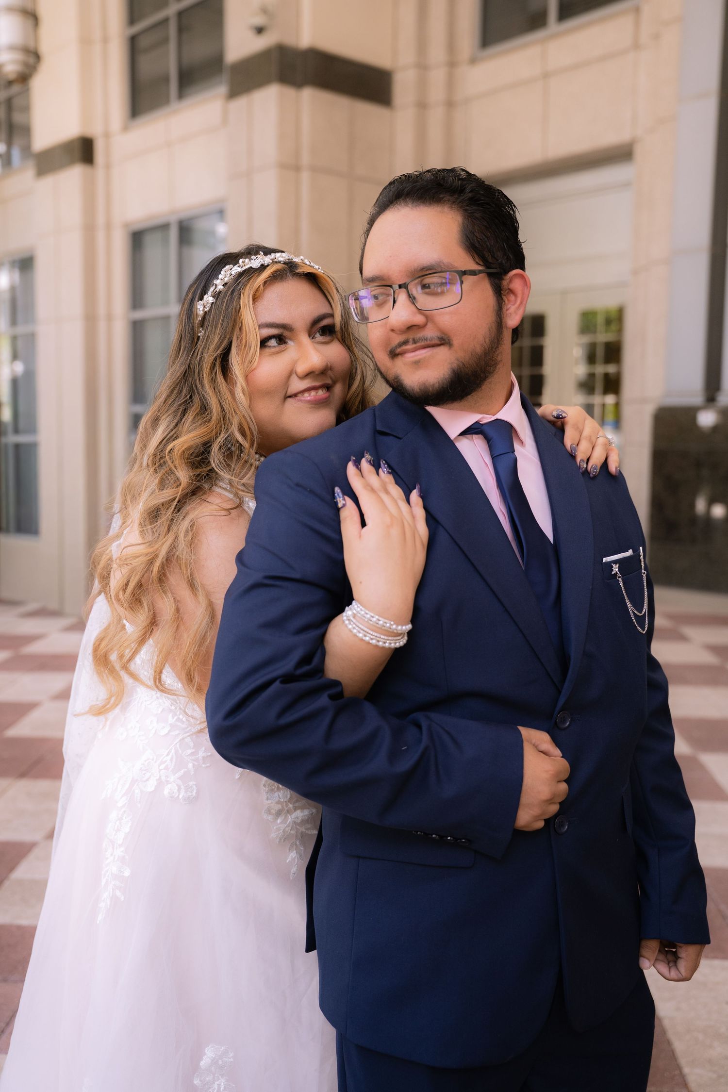 Bride and groom embracing outdoors, wearing white wedding dress and navy blue suit.