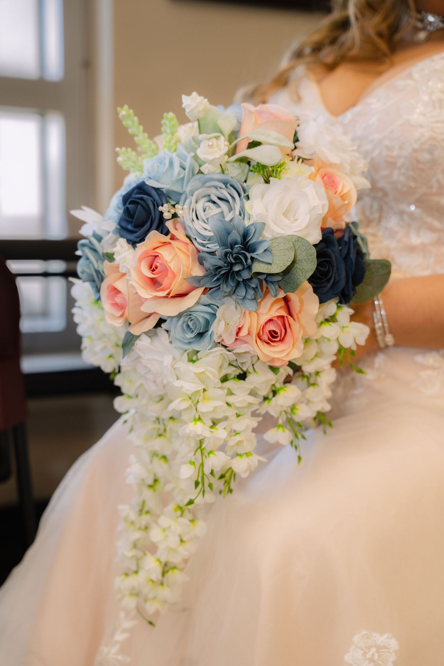 Bride holding a cascading bouquet of pink, blue, and white flowers in a wedding dress.