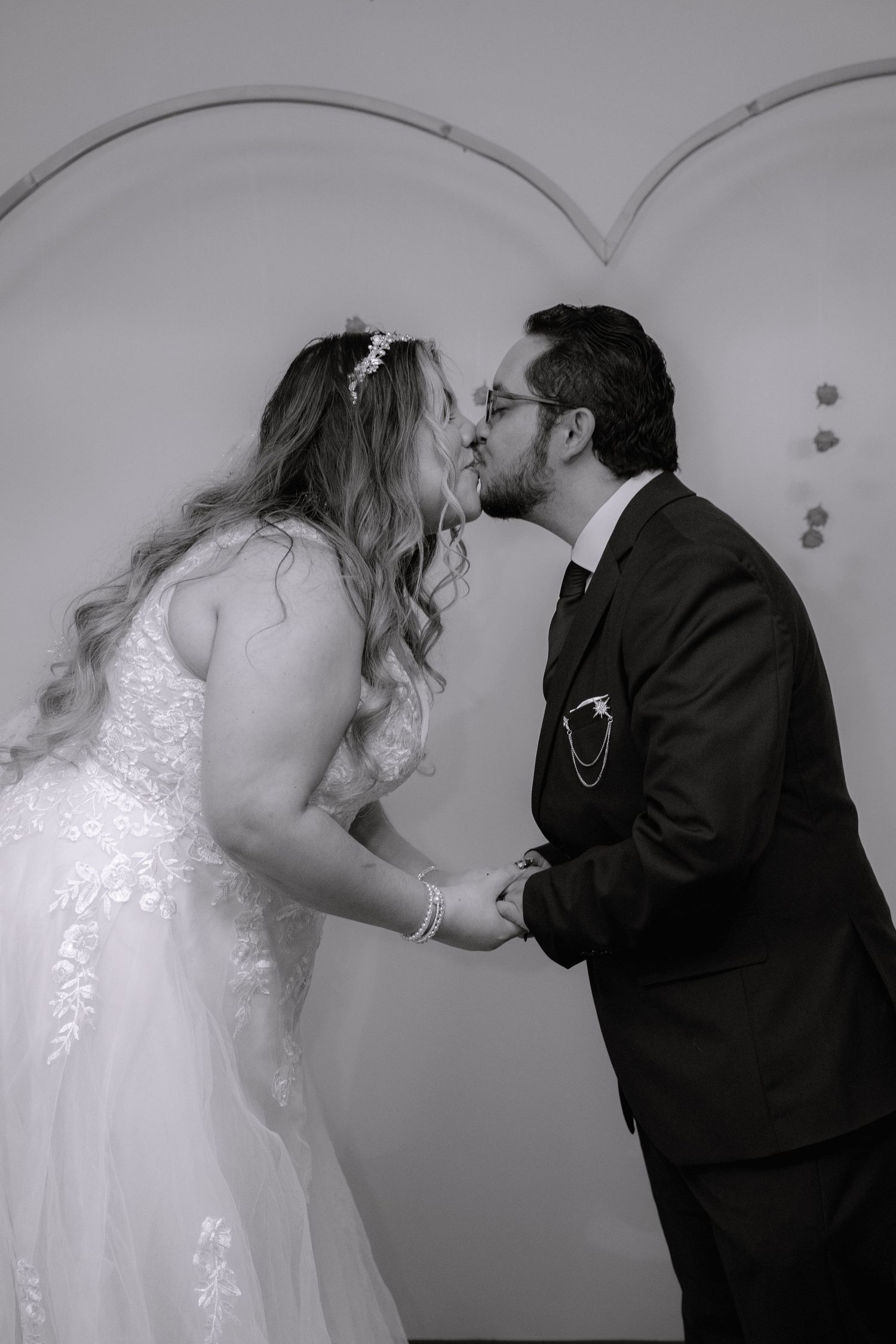 Black and white photo of bride and groom kissing under an arch indoors.