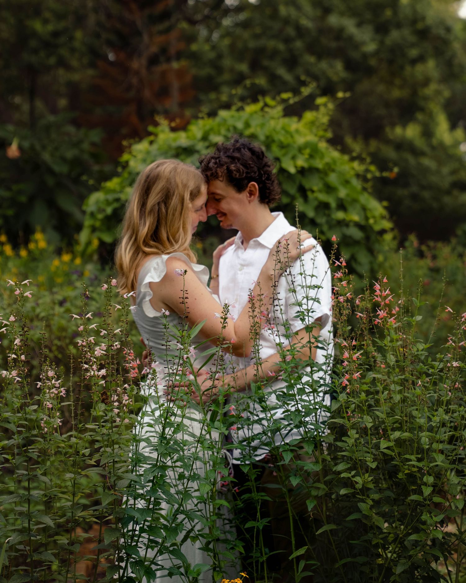 Romantic couple embracing face-to-face in a lush wildflower garden setting.