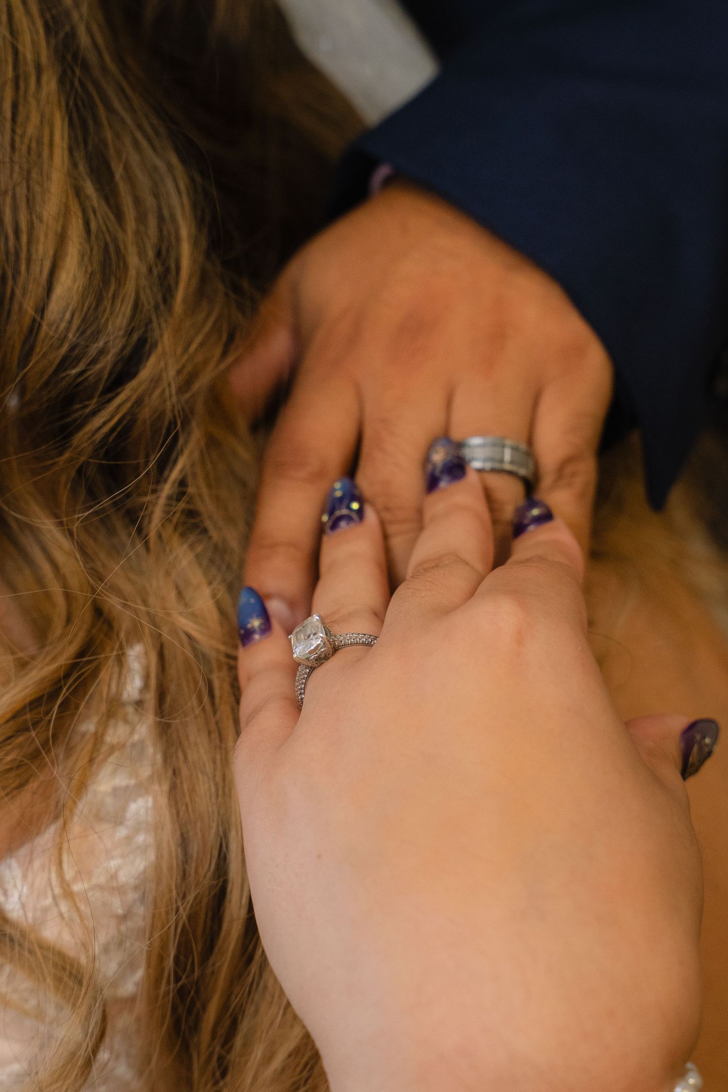 Close-up of bride and groom holding hands showing wedding rings with purple nail polish.
