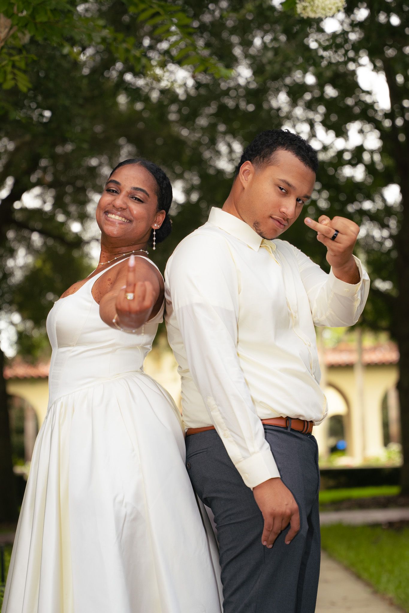 Bride and groom stand back-to-back proudly displaying their wedding rings to the camera.