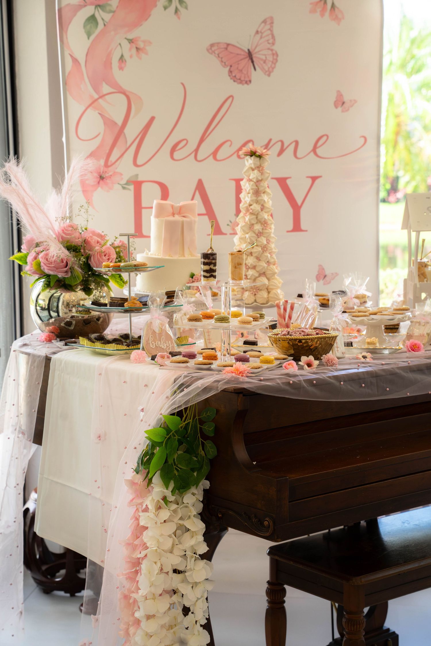 Welcome Baby shower dessert table with white cake, macaron tower, and pink butterfly backdrop.