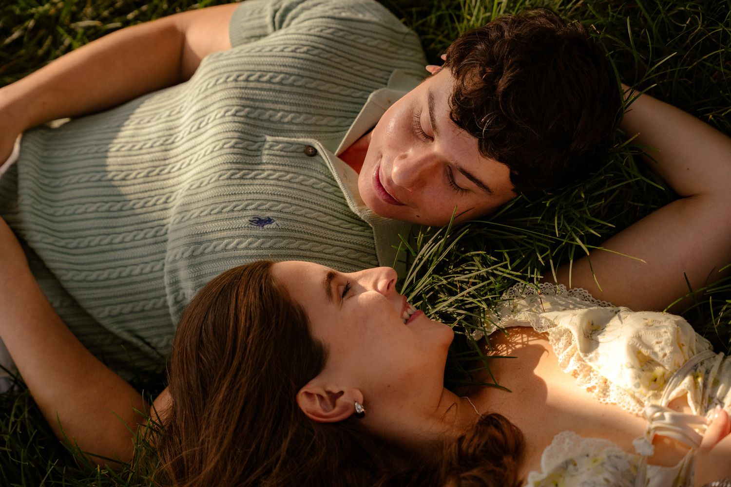 Romantic couple lying in green grass face to face, sharing a tender moment in golden light.