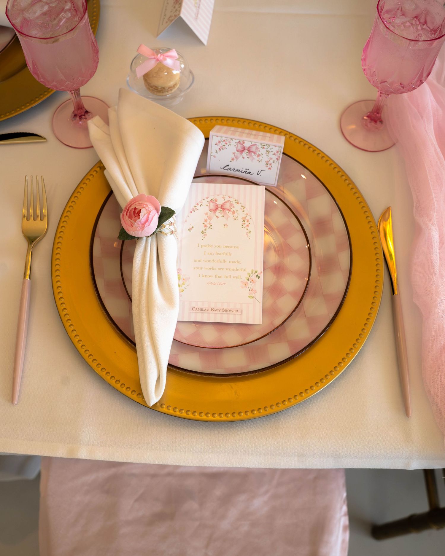 Elegant place setting with gold charger plate, pink rose napkin ring, and floral menu card.