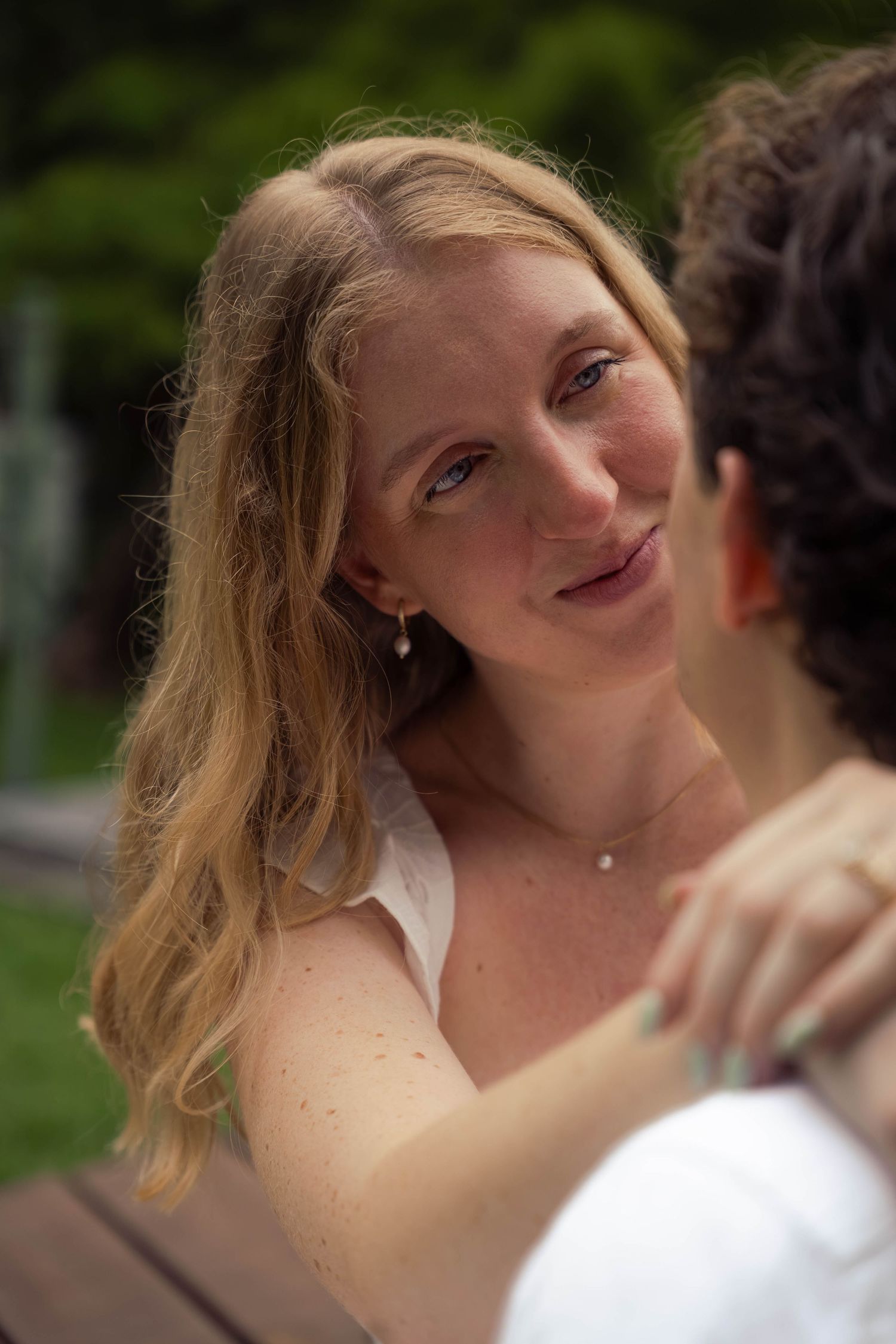 Woman with freckles and blonde hair smiling warmly at her partner outdoors.