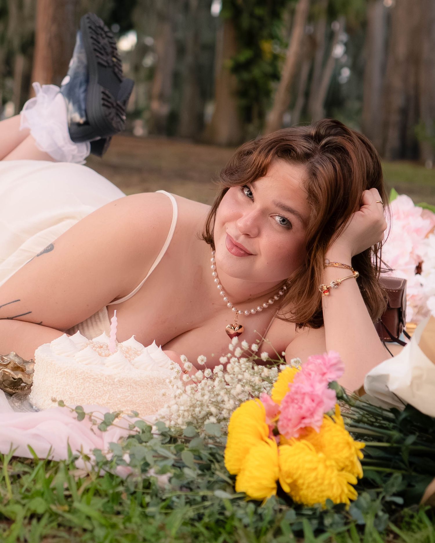 Woman in cream lingerie lying on grass surrounded by a white cake and flowers.