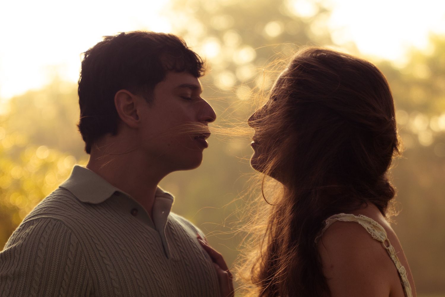 Young couple sharing an intimate almost-kiss moment outdoors in warm golden sunlight.