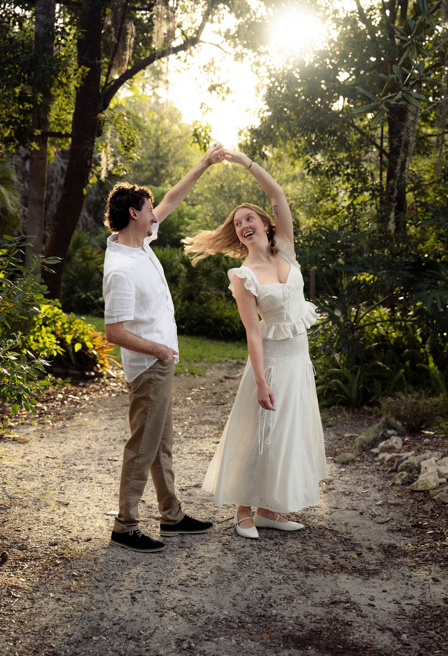 Couple dancing in golden sunlight on a forest path, woman spinning in white dress.