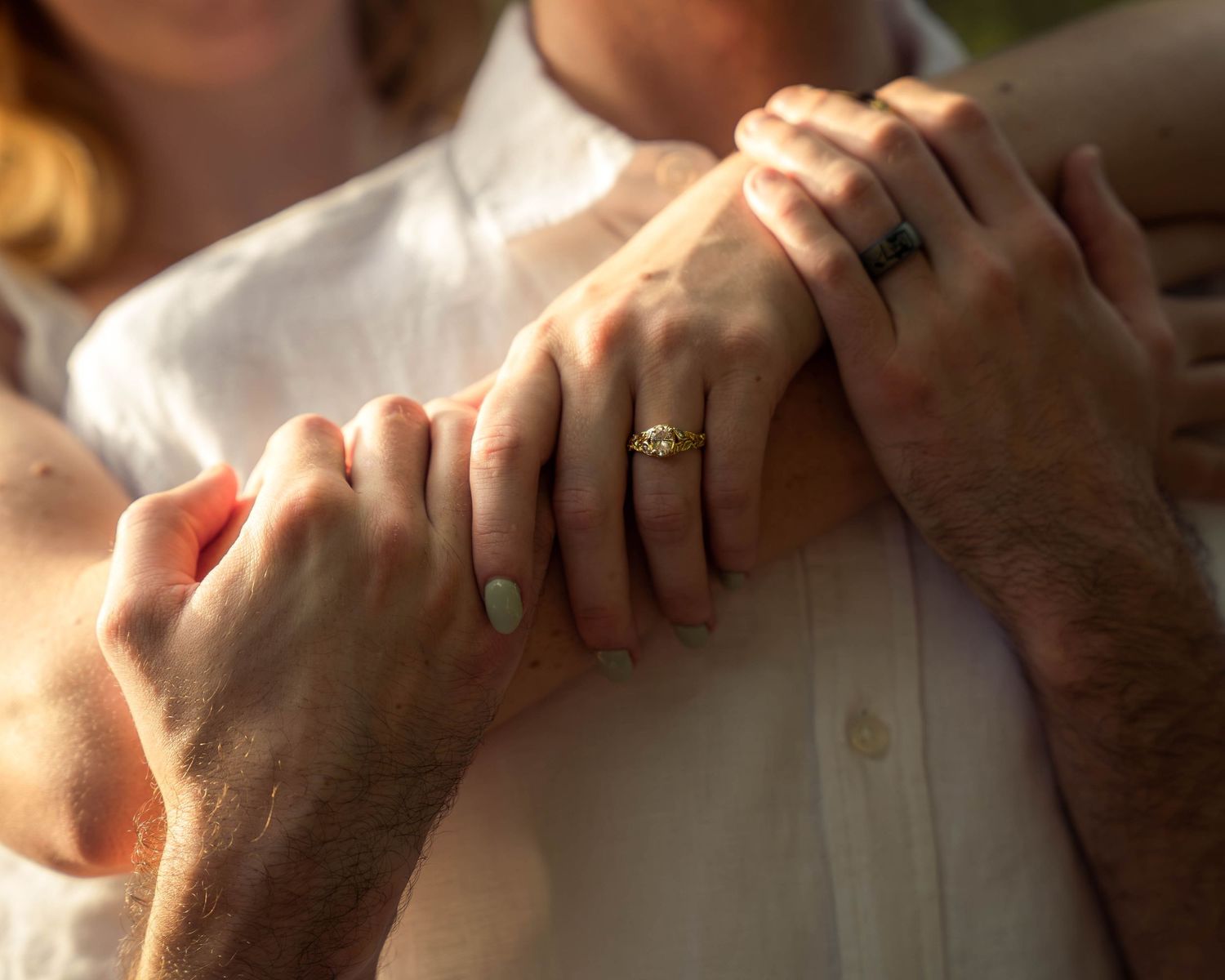Close-up of couple holding hands showing engagement and wedding rings outdoors.