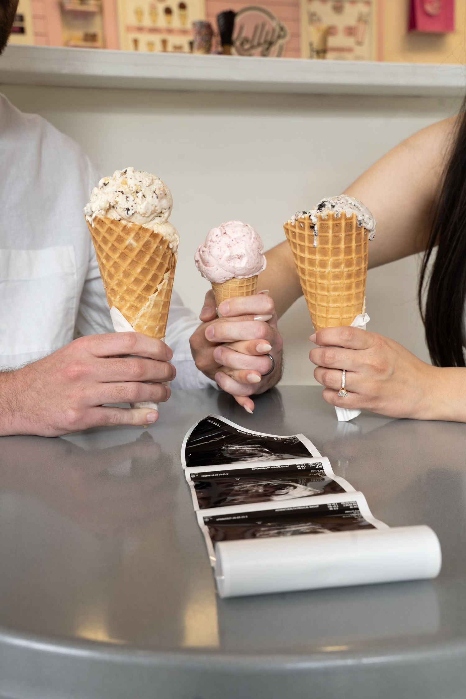 Couple holding three ice cream cones on waffle cones beside ultrasound photos on a table.