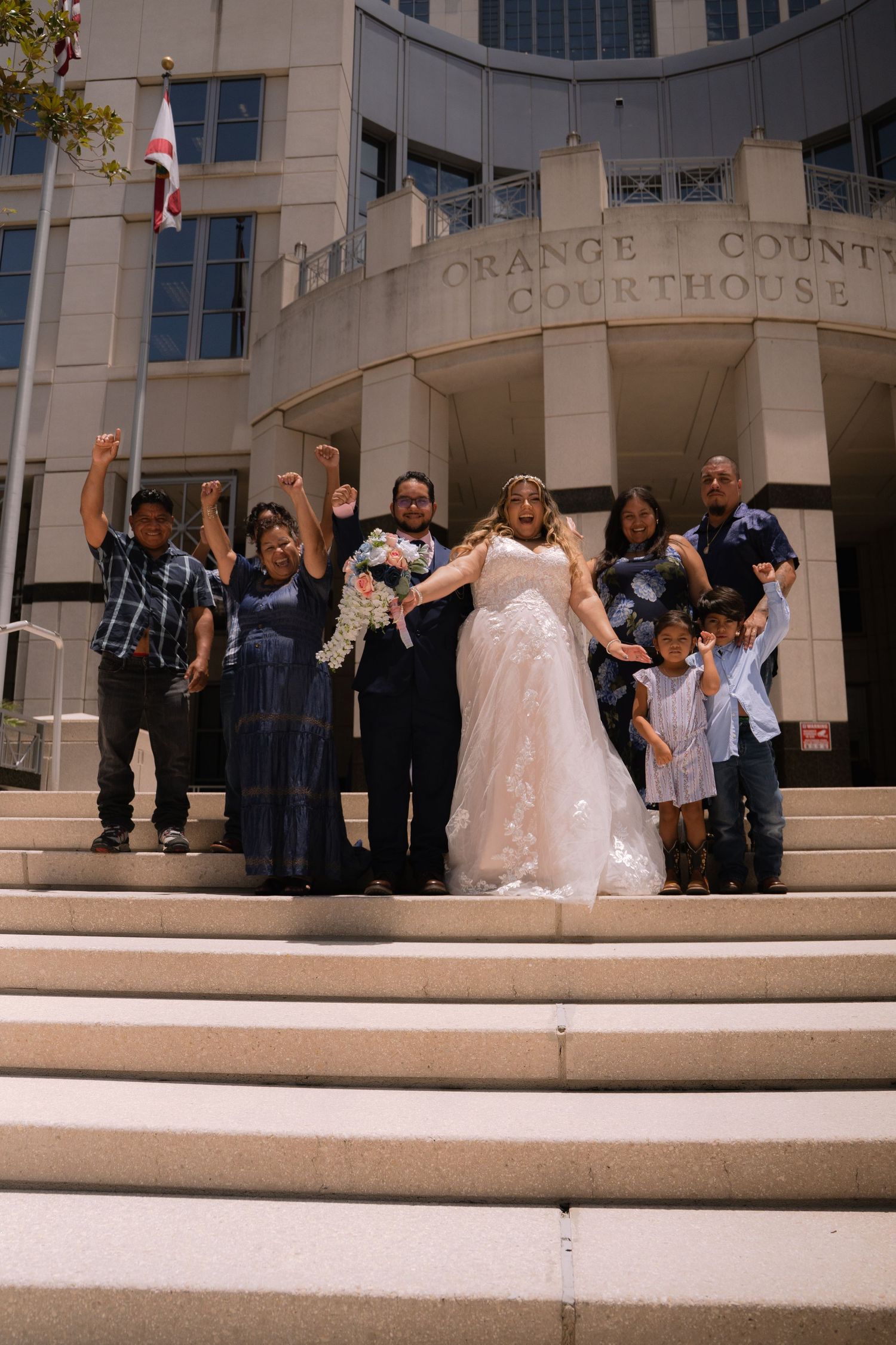 Joyful wedding party celebrates on Orange County Courthouse steps with raised arms after ceremony.