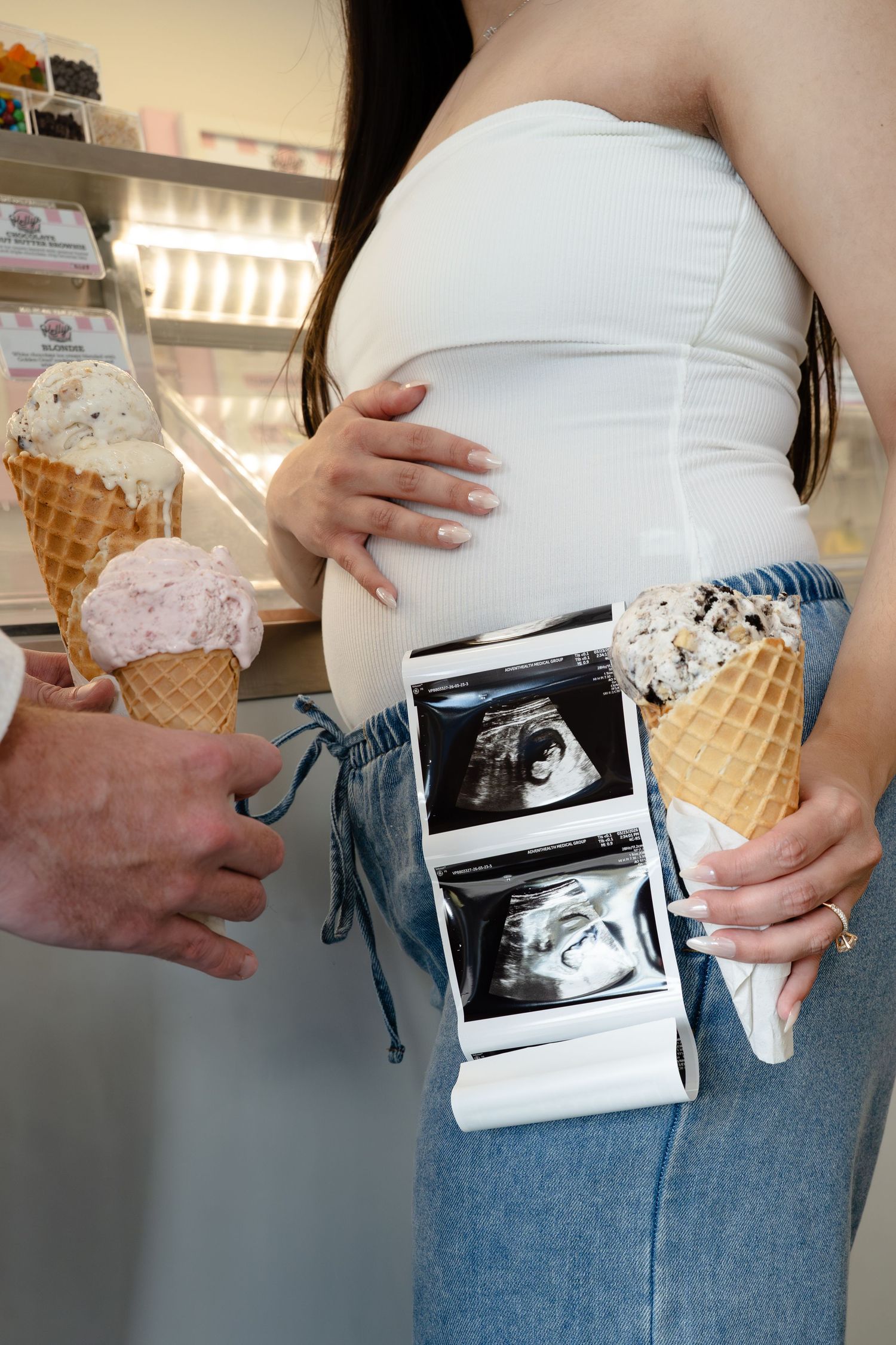 Pregnant woman holding ultrasound photos and ice cream cones in an ice cream shop.