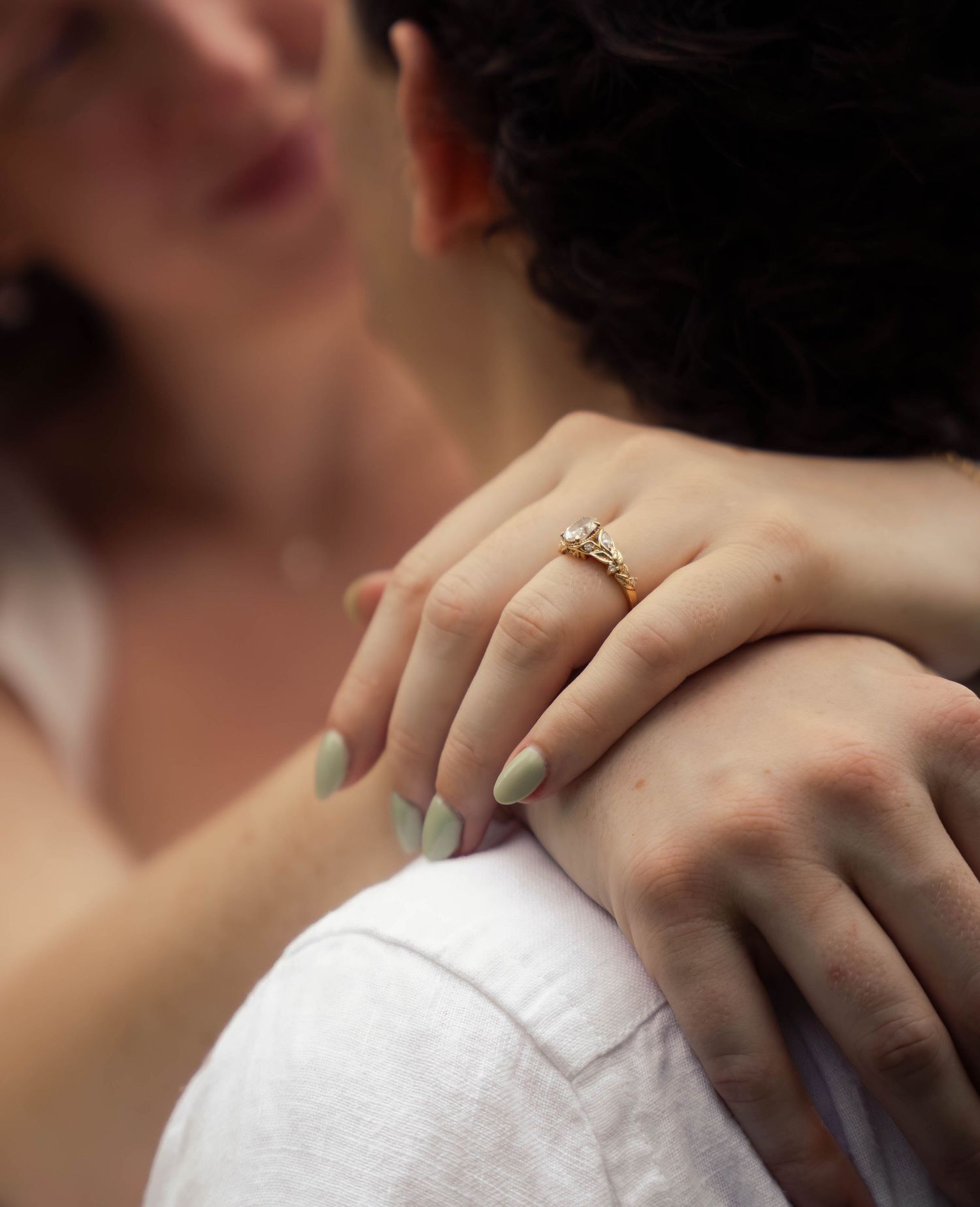 Close-up of woman's hand with mint nails and diamond engagement ring on partner's shoulder.