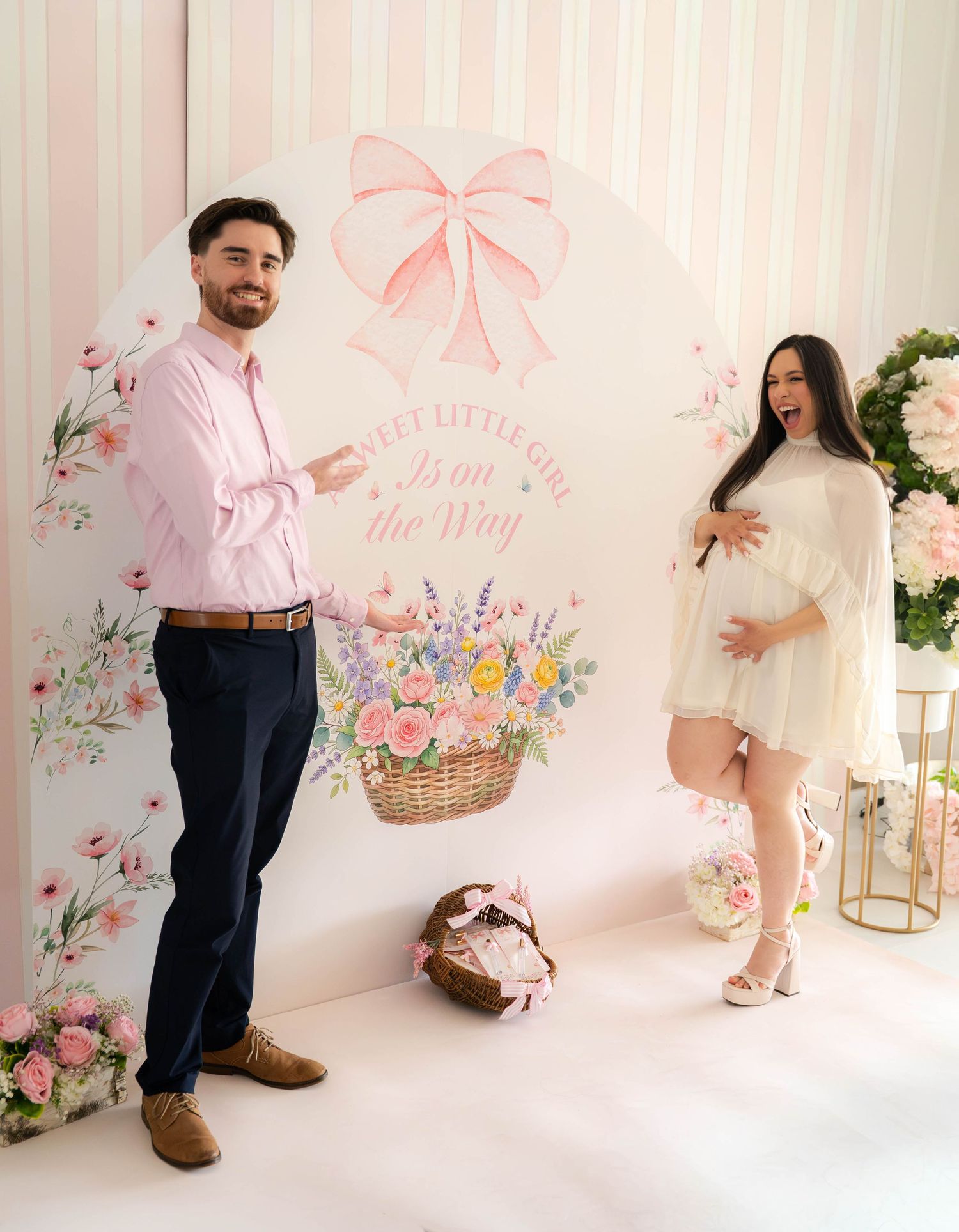Couple posing at a pink floral baby shower backdrop reading A Sweet Little Girl Is on the Way.