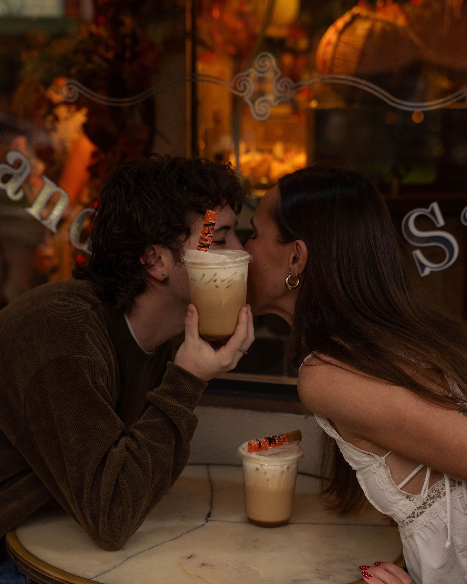 Couple sharing an iced coffee drink at a cafe table, leaning in close for a romantic moment.