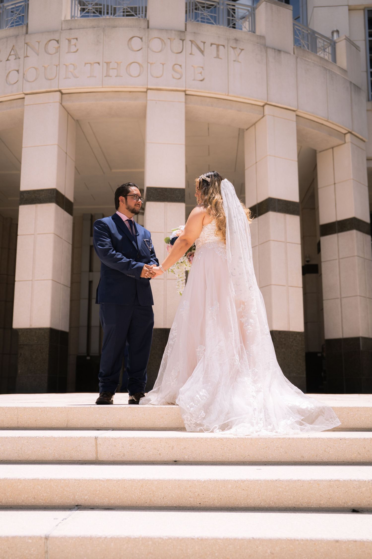 Bride and groom holding hands on courthouse steps, bride wearing long lace veil.