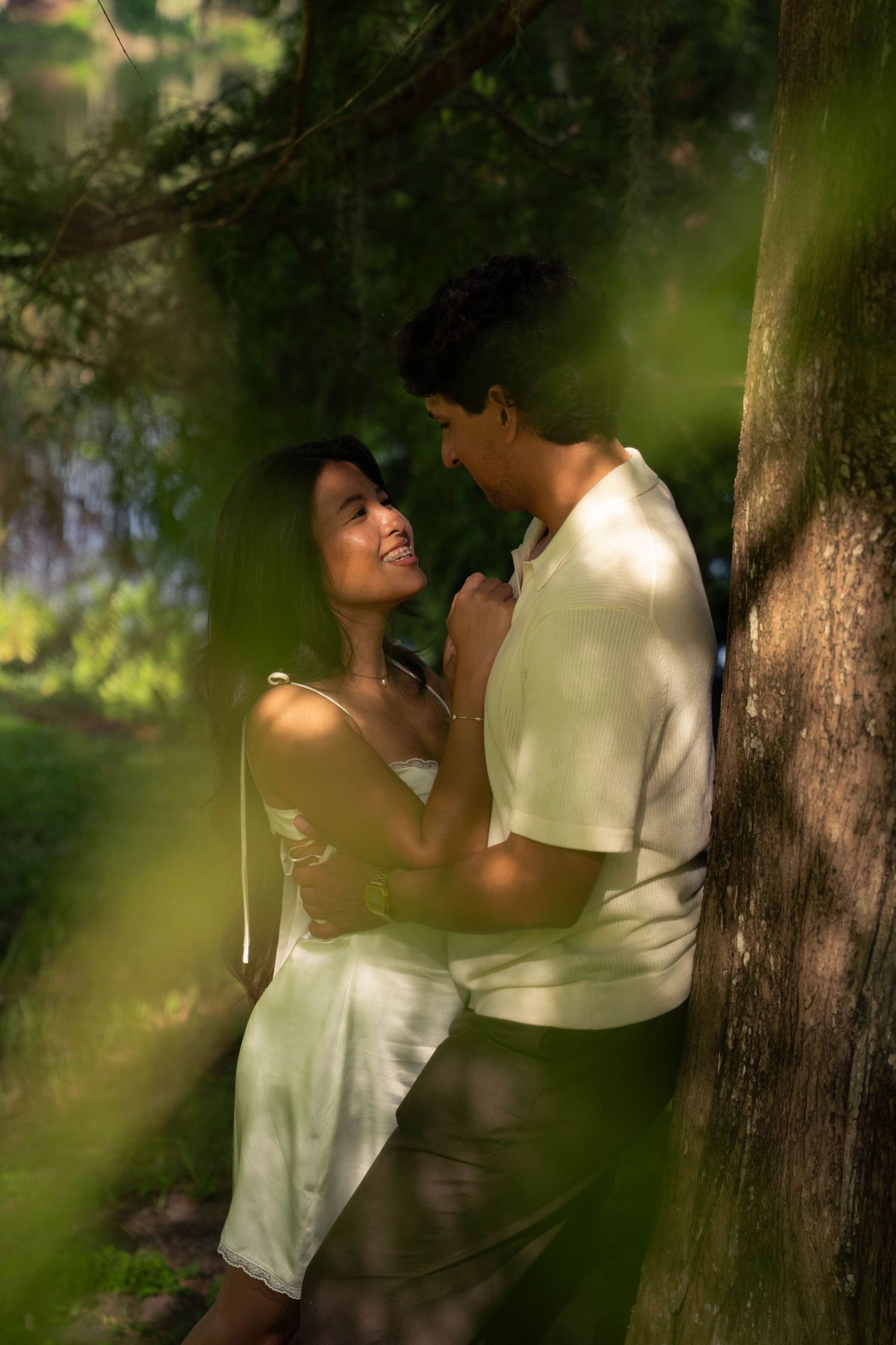 Couple sharing an intimate moment leaning against a tree in a lush green forest.