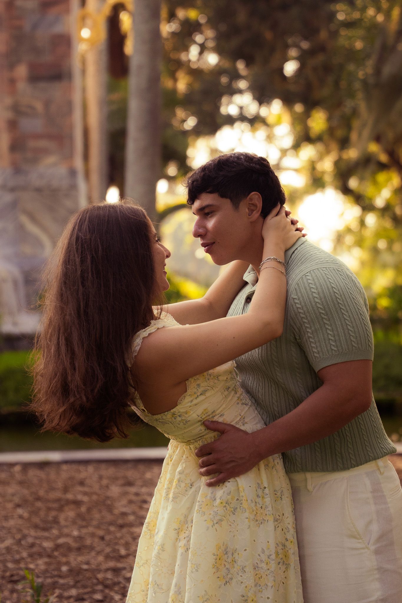 Couple embracing tenderly in a sunlit garden near historic stone architecture at sunset.