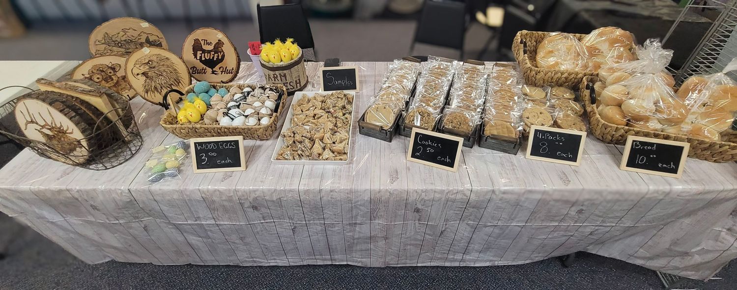 A rustic farmers market display table featuring an assortment of homemade baked goods and treats with chalkboard labels.