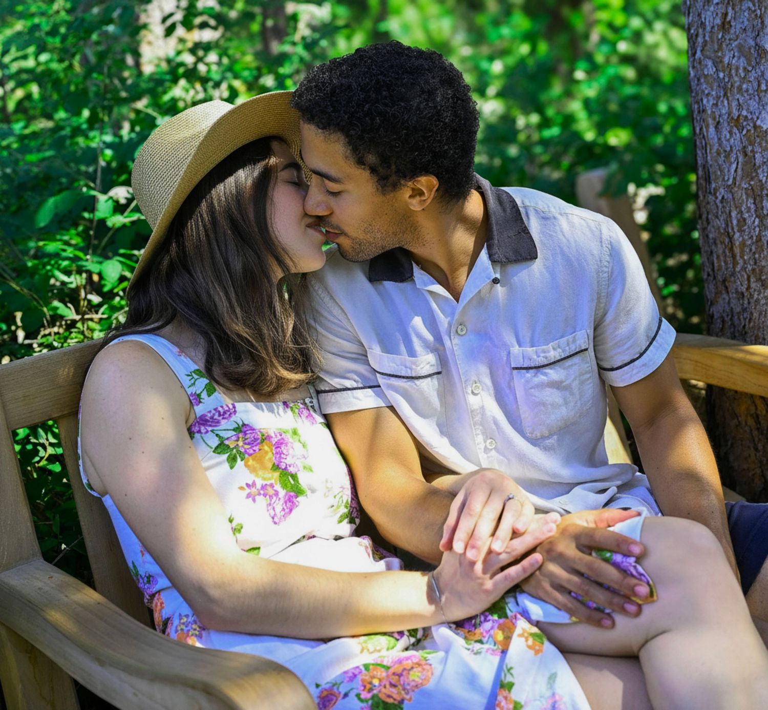 A young couple sharing a romantic kiss on a wooden bench surrounded by lush green trees outdoors.