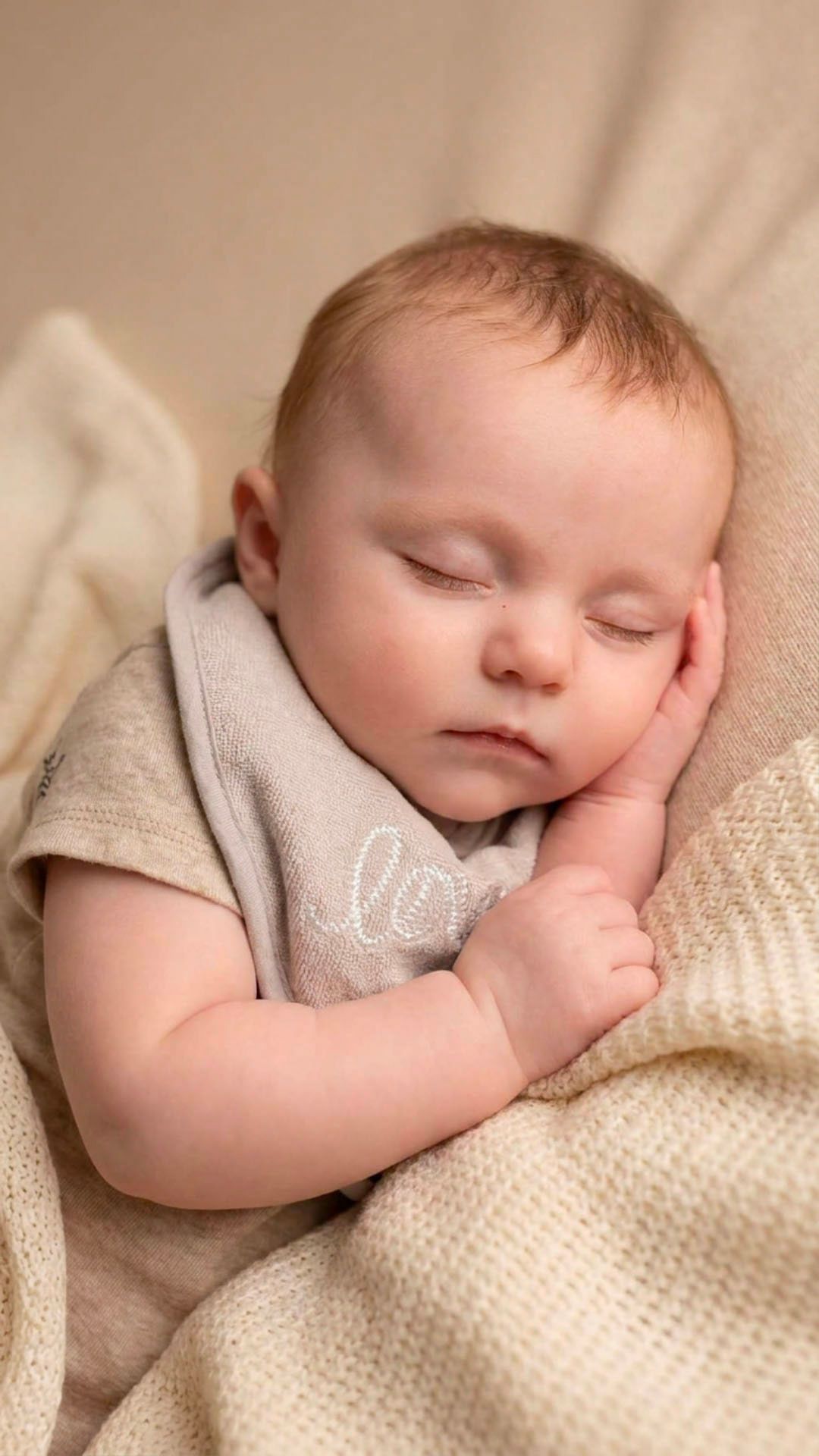 Peaceful newborn baby sleeping soundly, wrapped in a soft cream knit blanket, wearing a gray onesie.